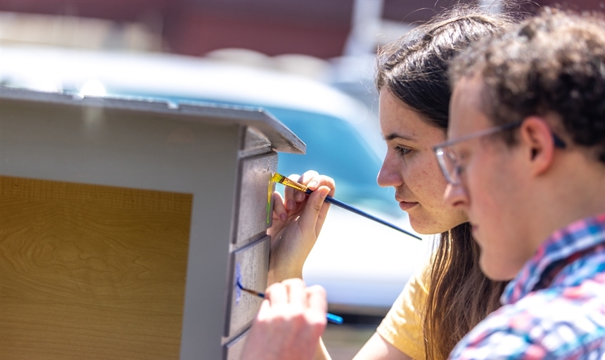 two students painting a bird house