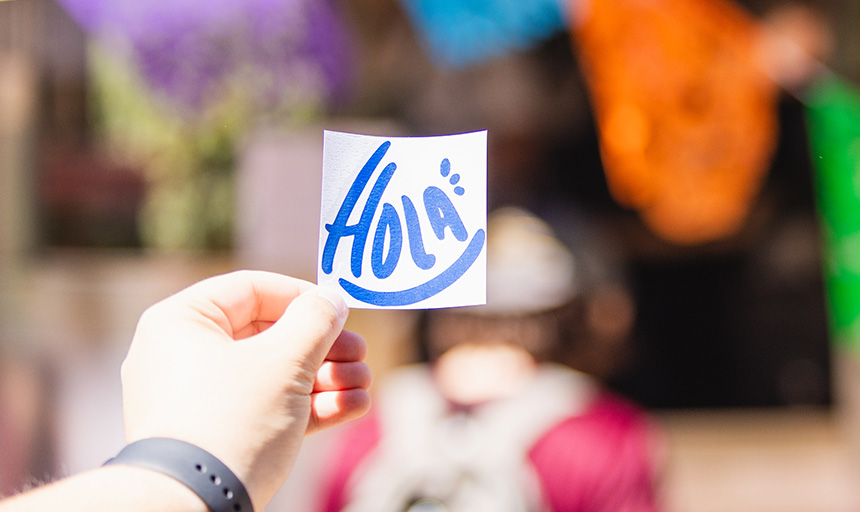 A hand holding up a sticker with the HOLA logo