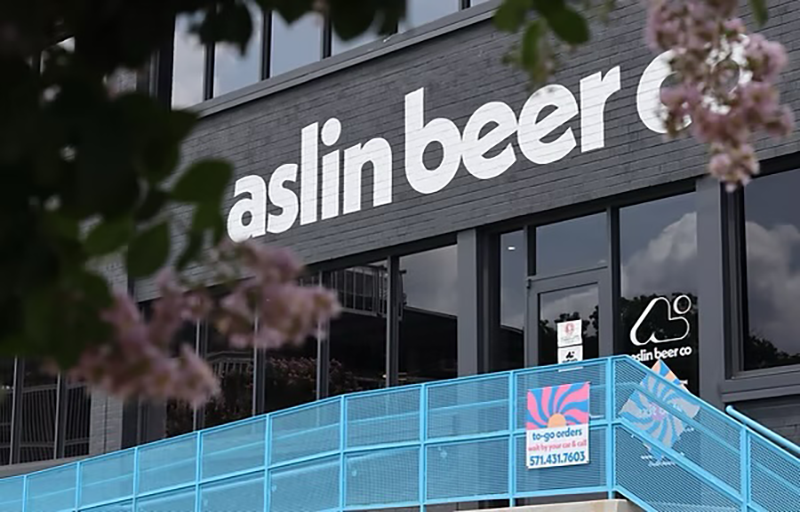 Outside of aslin beer company featuring a bright blue metal fence, cherry blossoms and the words aslin beer written on a black building