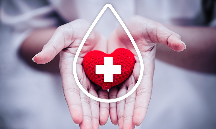 Hand holding a small, crocheted figure in the shape of a red heart with a white cross over it