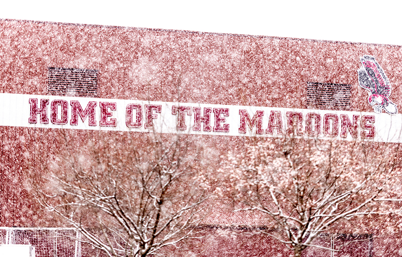 snow falling with the backdrop of a building reading "Home of the Maroons"
