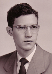 Black and white headshot of a young man with glasses in suit and tie.