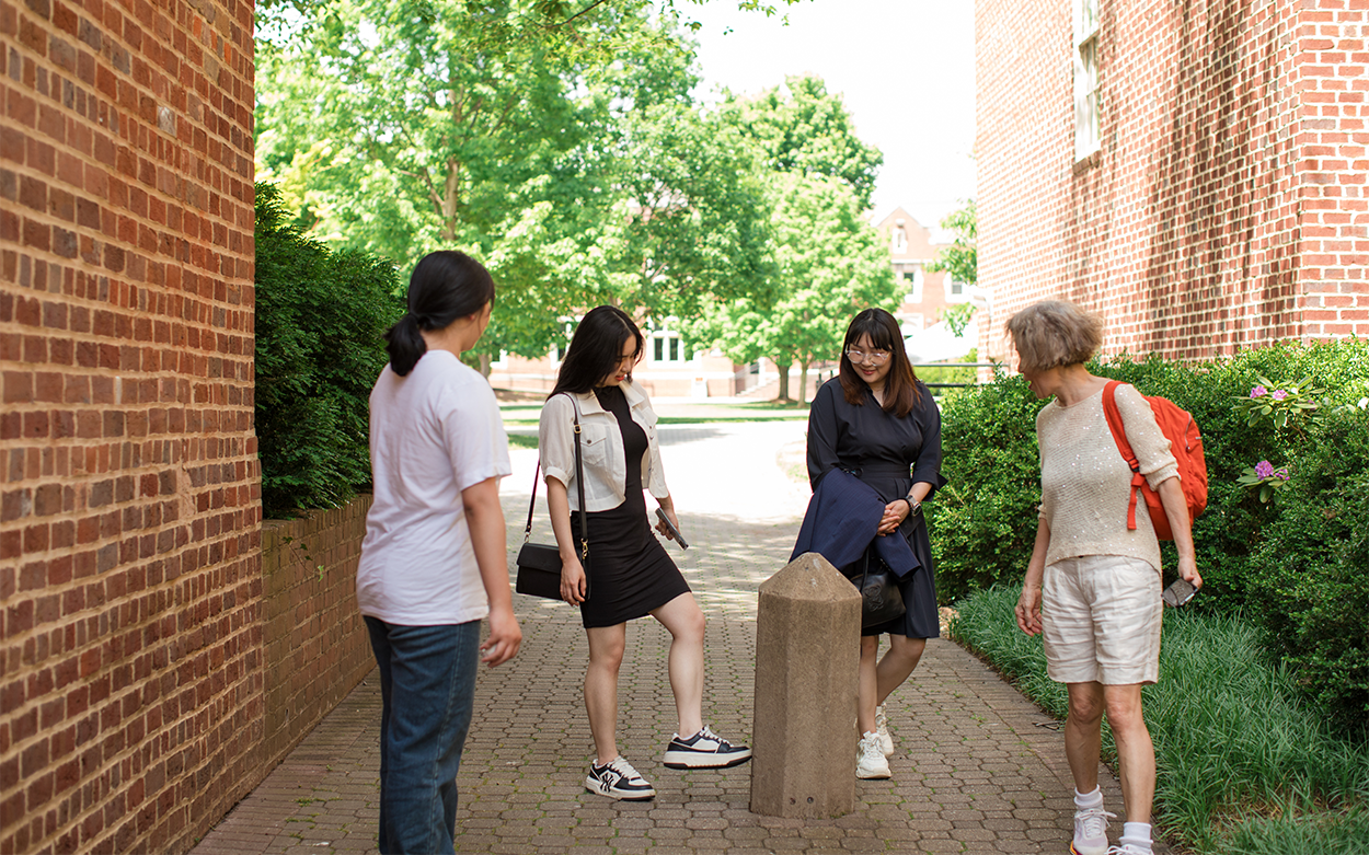 Four people stand around a concrete obelisk as two of them kick it
