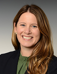 Headshot of a brown-haired woman in a green blouse and black blazer