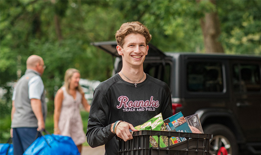 A student smiles while carrying a box