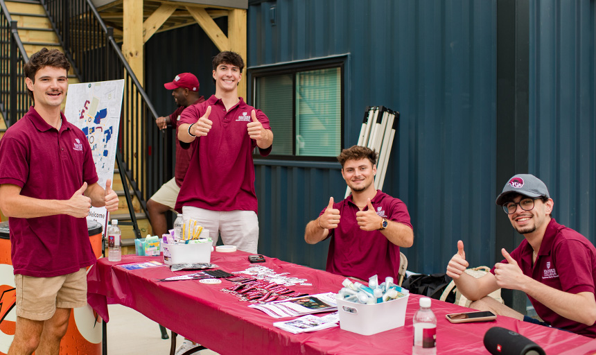 Student resident advisors smile and give a thumbs up to the camera