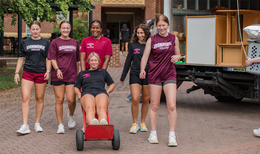 Students laugh while carting a fellow student around on a moving dolly