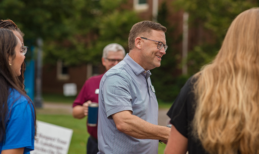 The college president smiles while talking with students