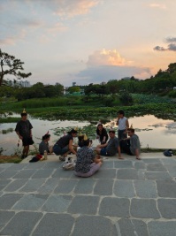 Group of young people in birthday hats celebrate next to a pond with the sun setting on the water.