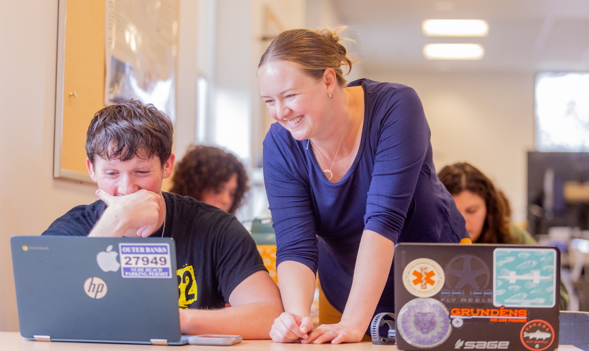 A professor helps a student who is working at a laptop