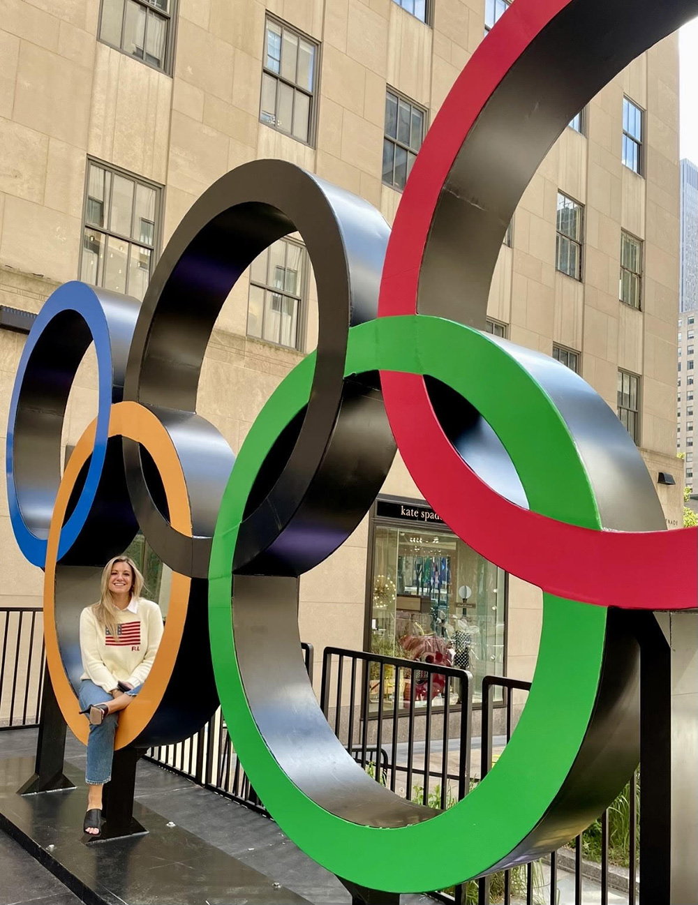 Woman sits inside one ring of a large display of Olympic rings.