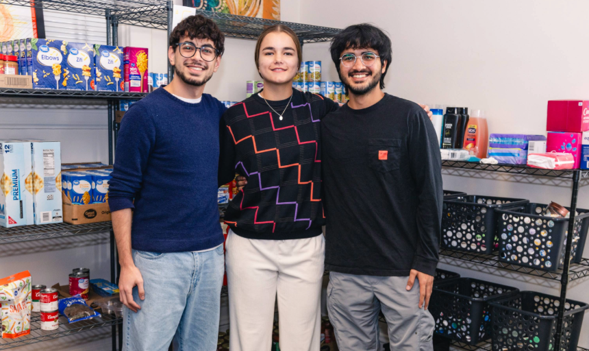 Three students smiling for a photo in front of shelves of food