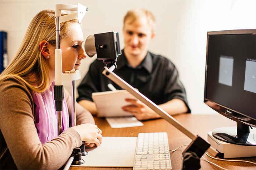 A student peers through an eye device and reads directions on a nearby computer screen during an experiment